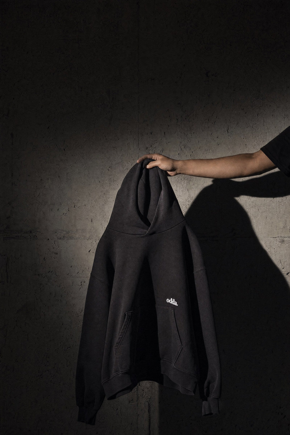 Black Odda heavyweight hoodie held up against a concrete wall